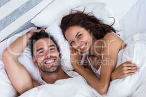 High angle portrait of cheerful couple relaxing on bed
