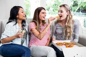 Beautiful young female friends enjoying wine and pizza