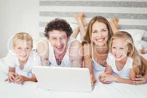 Smiling family using laptop on bed