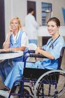 Portrait of smiling doctor sitting on wheelchair with colleagues