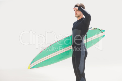 Man with surfboard shielding eyes at beach