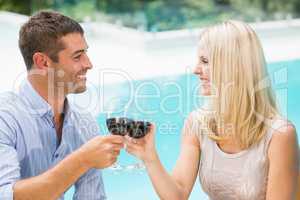 Smiling couple toasting red wine while sitting by swimming pool