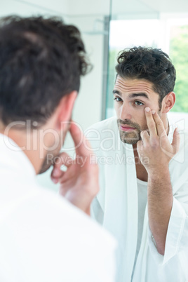 Man checking eyes in bathroom mirror