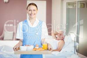 Portrait of cheerful nurse with tray standing in room
