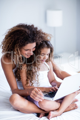 Mother and daughter using laptop on bed