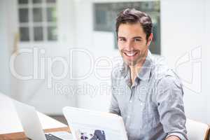 Smiling young man holding documents while sitting at desk with l