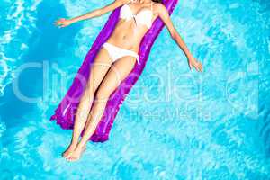 Woman in white bikini lying on air bed in pool