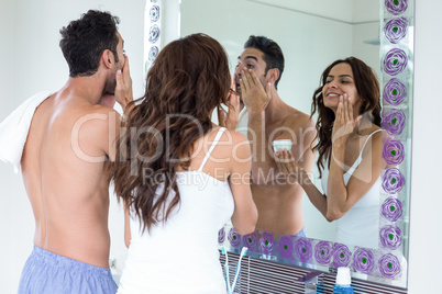 Couple applying cream on face while looking in mirror