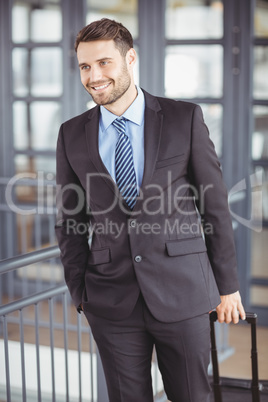 Handsome businessman walking with luggage by railing