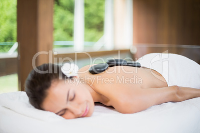 Woman lying on massage table with spa stones at back