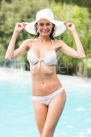 Woman in bikini smiling while standing by swimming pool