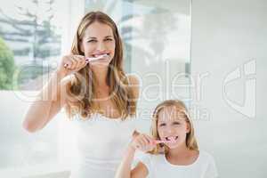 Portrait of happy mother and daughter brushing teeth