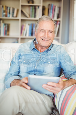 Portrait of senior man using tablet while sitting on sofa