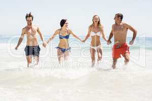 Happy friends holding hands and running on the beach