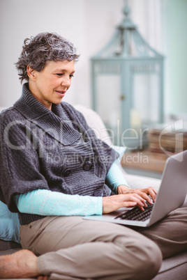 Mature woman using laptop while sitting on sofa Mature woman using laptop while sitting on sofa