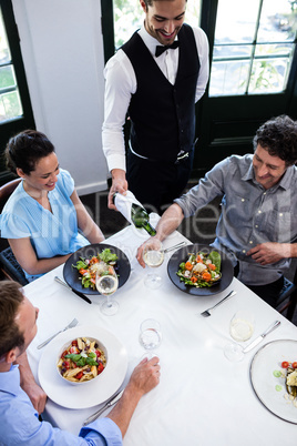 Waiter serving wine to group of friends while having lunch