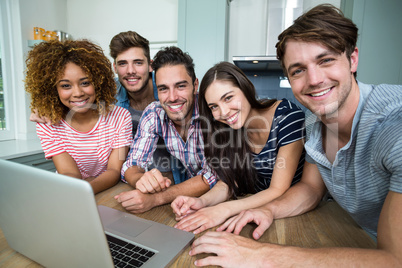 Multi-ethnic friends smiling while using laptop on table
