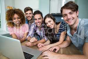 Multi-ethnic friends smiling while using laptop on table