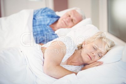 Senior woman sleeping besides husband on bed