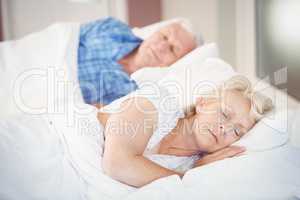 Senior woman sleeping besides husband on bed