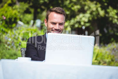 Smiling businessman using laptop and having a coffee