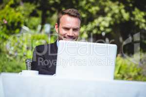 Smiling businessman using laptop and having a coffee