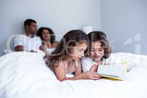 Brother and sister reading book together on bed