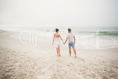 Rear view of couple holding hands and walking on the beach