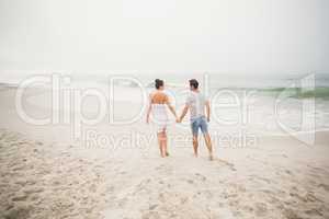 Rear view of couple holding hands and walking on the beach
