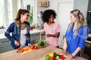 Female friends smiling while preparing food in kitchen
