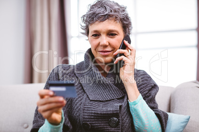 Mature woman holding credit card while talking on mobile phone