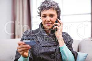 Mature woman holding credit card while talking on mobile phone