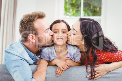 Mother and father kissing daughter at home
