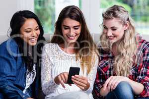 Female friends looking in mobile phone while sitting at home