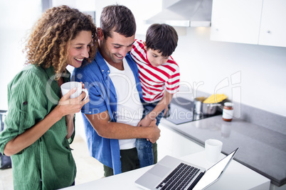 Parents using laptop with son in kitchen Parents using laptop with son in kitchen