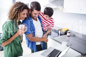 Parents using laptop with son in kitchen