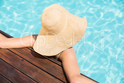 Woman wearing straw hat leaning on wooden deck by poolside