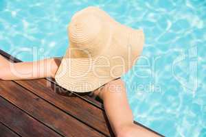 Woman wearing straw hat leaning on wooden deck by poolside