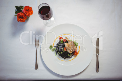 Squid ink spaghetti dish with basil with flowers and red wine