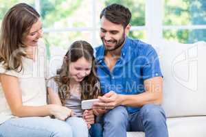 Family looking at smart phone while sitting on sofa