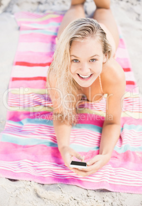 Happy woman lying on the beach and using mobile phone