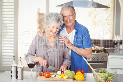 Happy senior man standing with woman cutting salad