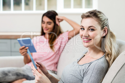 Happy woman using digital tablet while female friend in backgrou