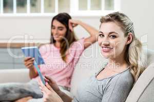 Happy woman using digital tablet while female friend in backgrou