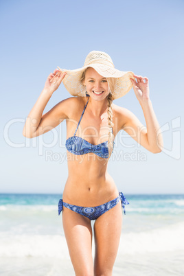 Pretty woman in bikini and beach hat standing on the beach