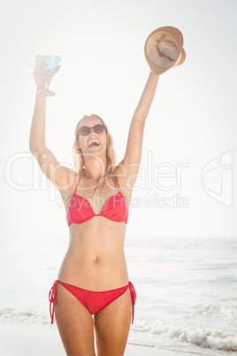 Excited woman with a cocktail drink standing on the beach