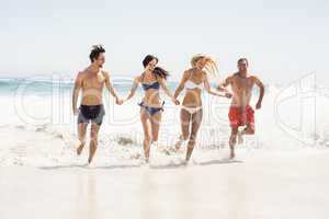 Happy friends holding hands and running on the beach