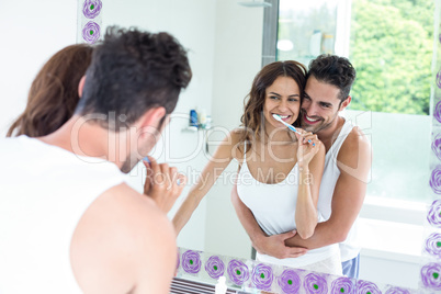 Woman brushing teeth while husband embracing her in bathroom