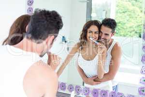 Woman brushing teeth while husband embracing her in bathroom