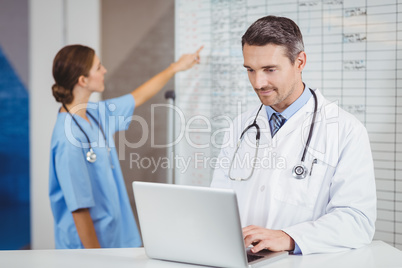Doctor working on laptop with colleague pointing at chart